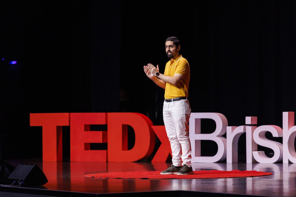 Danish Kazmi standing in the red circle on stage delivering his TEDx Talk at TEDxBrisbane.