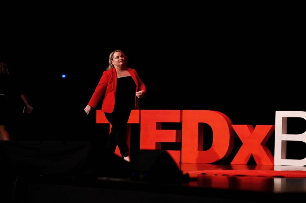 Juanita walking onto stage wearing a red jacket as host of TEDxBrisbane 2022.